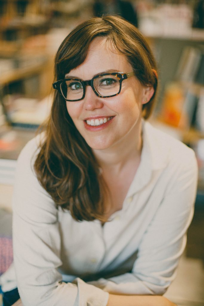 Caroline Donahue looks at camera, smiling and wearing glasses.